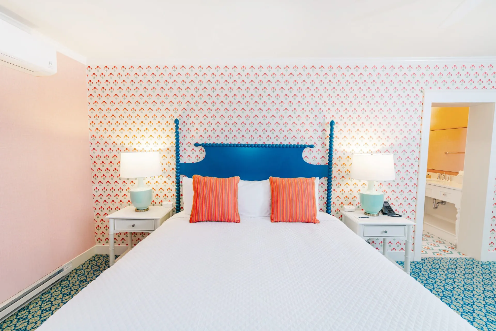 A pink polka dot room with patterned green carpet showcasing a bed with lamps.