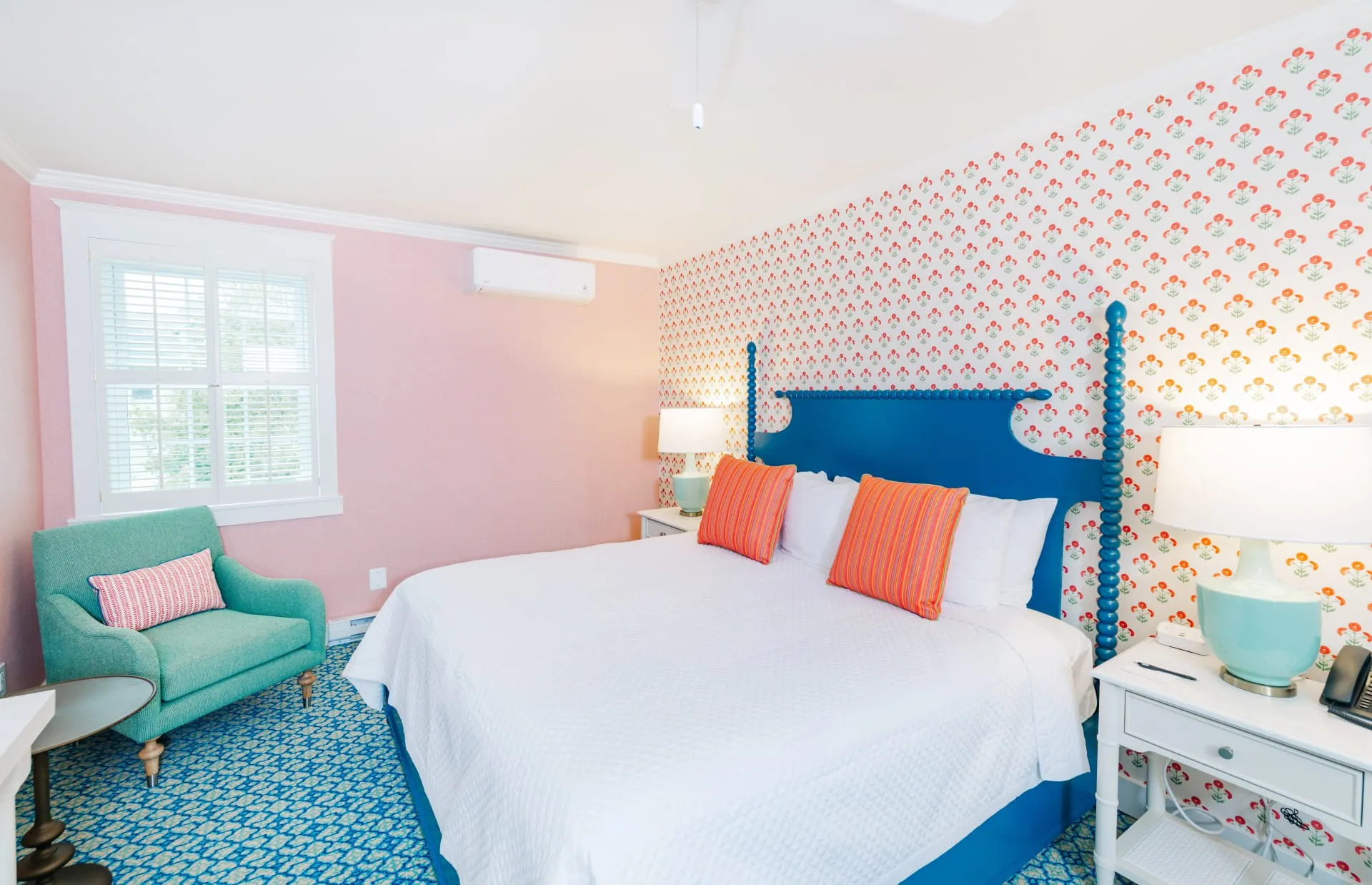A pink room with polka dot with green pattern, green chair, and blue bed with white mattress.