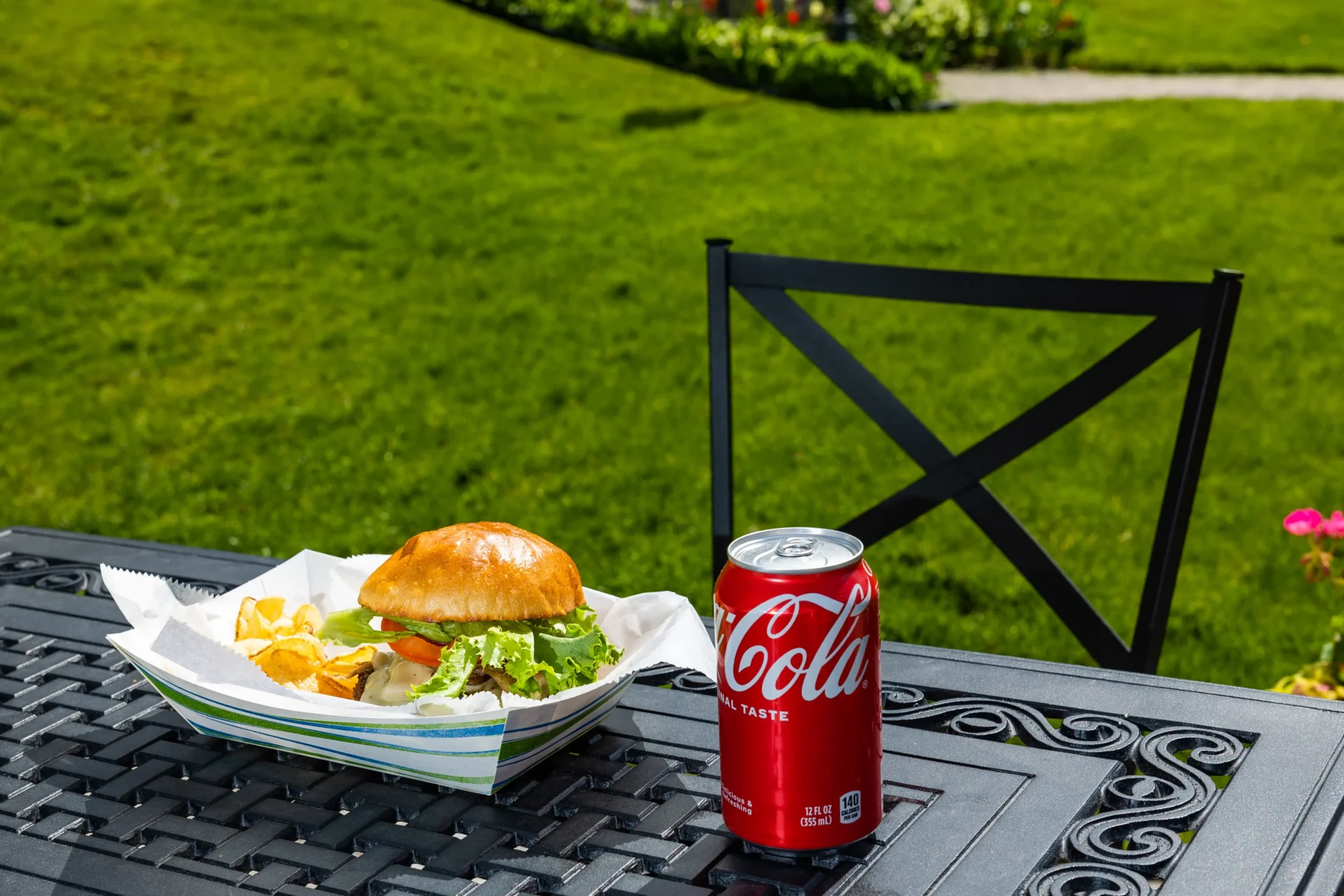 A burger with a can of Coca-Cola on a table in the front lawn.