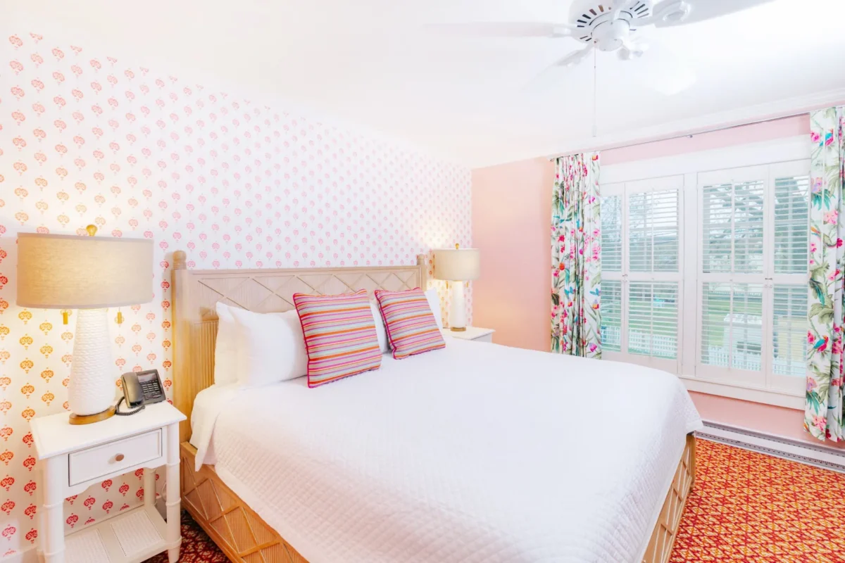 Pink polka dot room with orange carpet and white bed in front of a window.